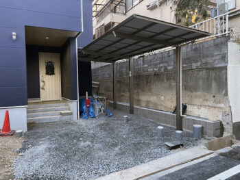 高槻市のM様邸外構カーポートは三協アルミのセラフィです隣地との擁壁の間にはユニソンのリゲルというぬろっくを使っています。建物の奥へ向かう通路は見切って奥を砕石で仕上げてカーポートの下はこのあとガレージ土間で仕上げていきます