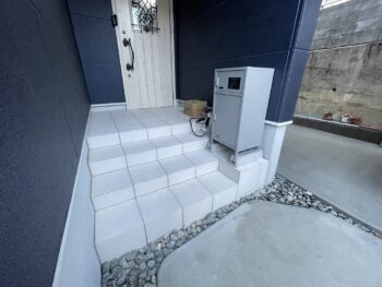 高基礎の玄関だったのでポーチ含めて4段の玄関ポーチを作り白い大判タイルで仕上げました。宅配ボックスも安定して置けるよう施工しています