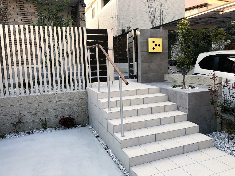 大判タイルの階段アプローチに黄色いポストがアクセントシンボルツリーの植栽スペースはタイルに穴を開けたようなデザイン